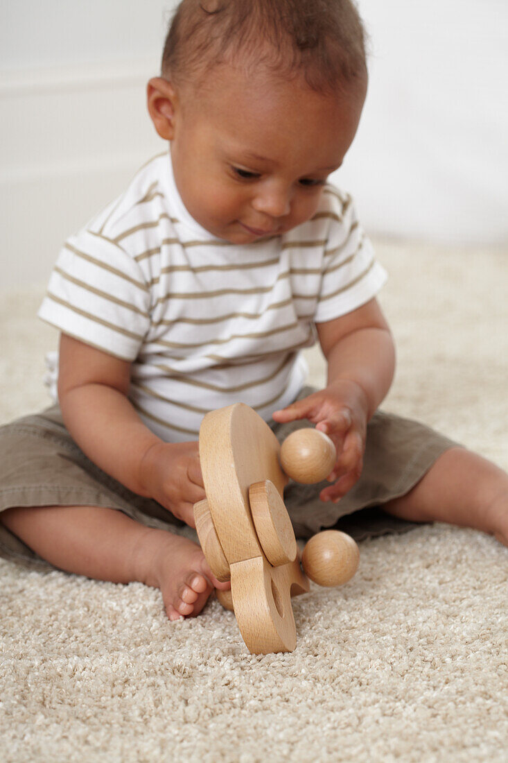 Baby boy sitting on carpet playing with wooden toy