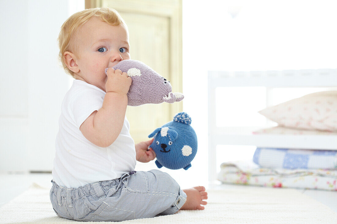 Baby boy playing and chewing soft knitted animal toys