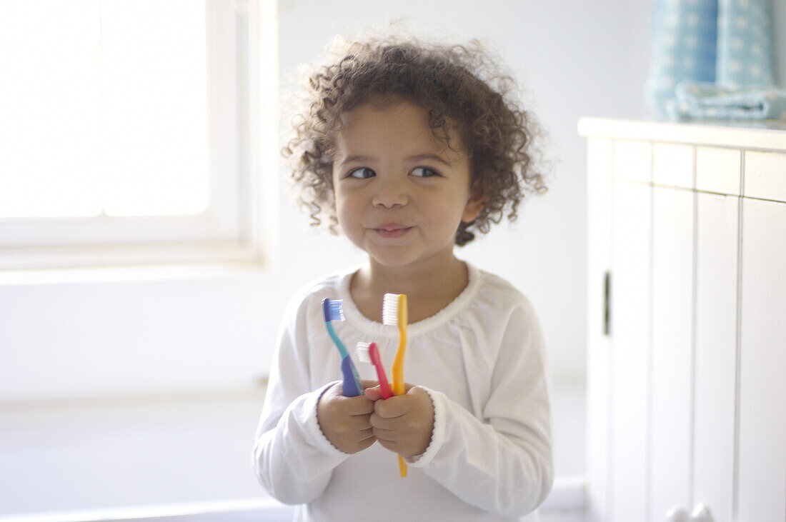 Girl holding three different coloured toothbrushes