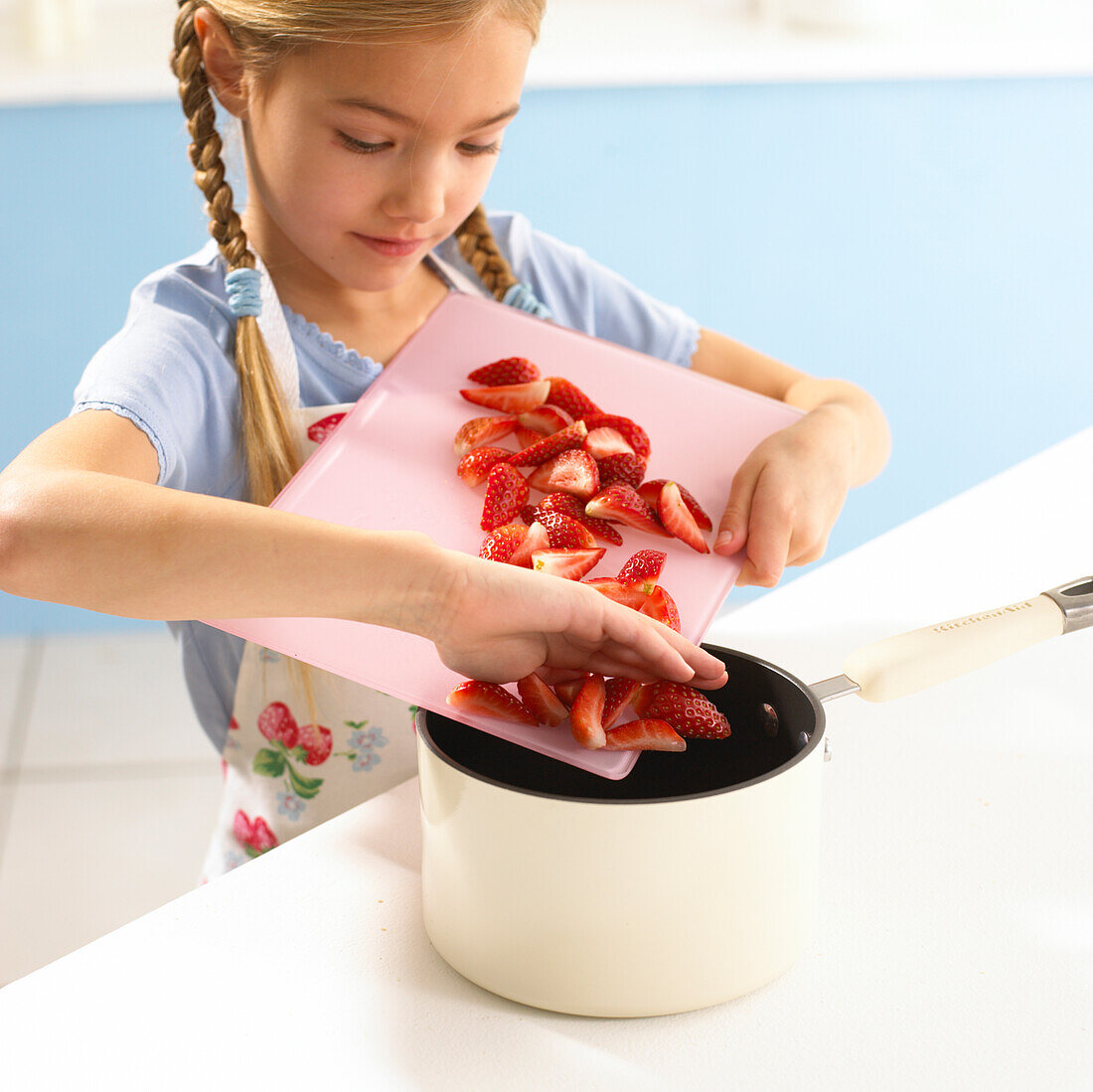 Girl sliding chopped strawberries into a saucepan