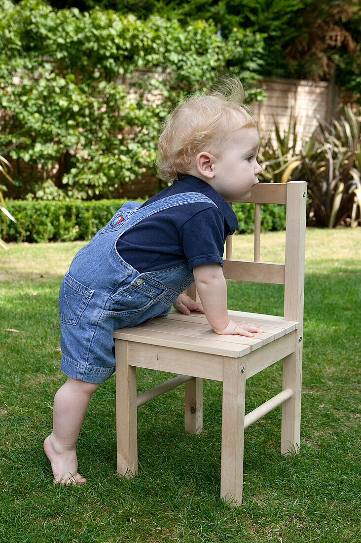 Baby boy climbing onto wooden chair in a garden