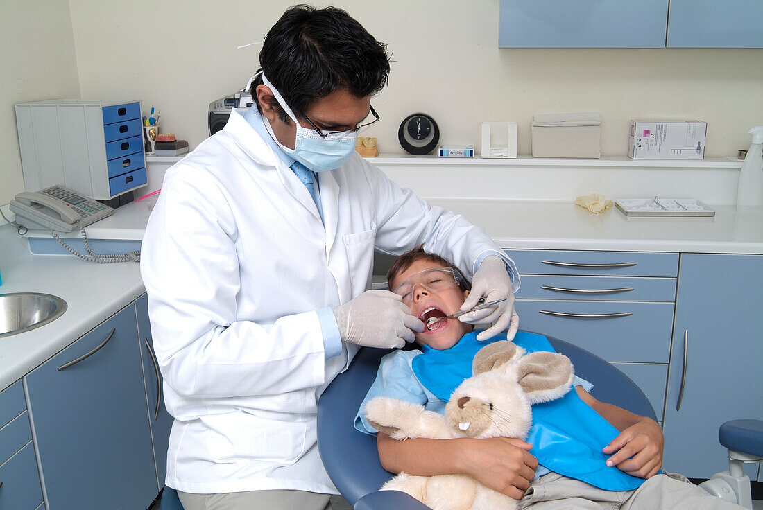 Dentist wearing mask holding mirror in boy's mouth