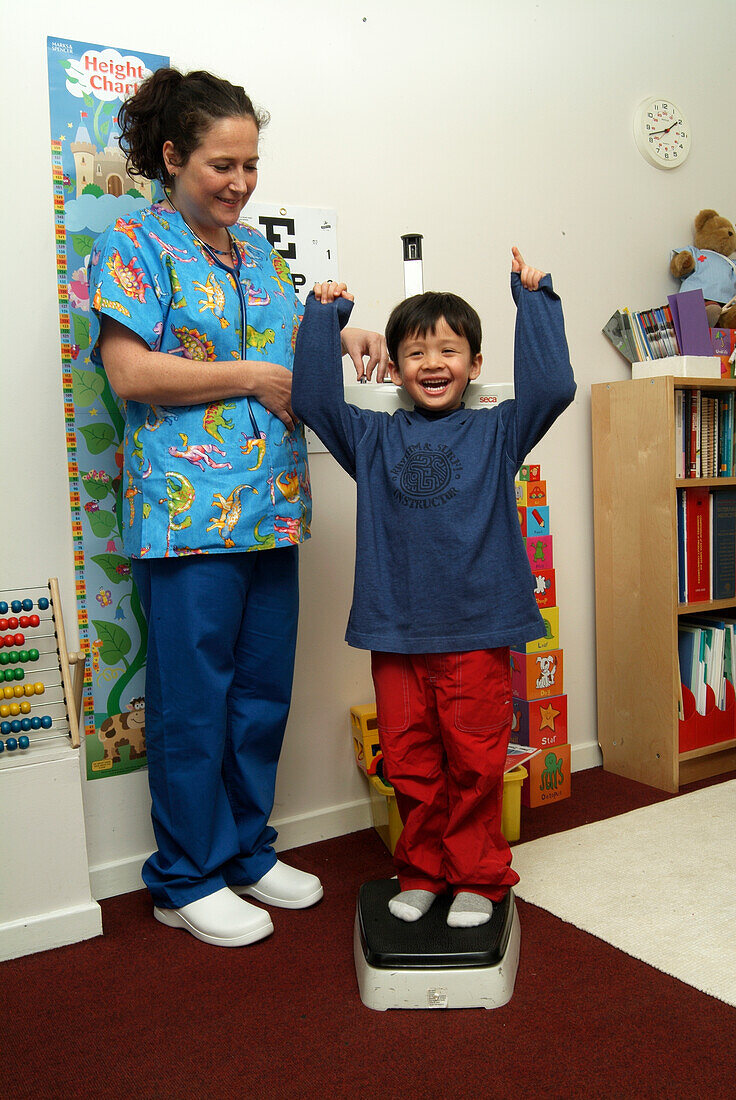 Boy standing on scales with arms raised next to nurse