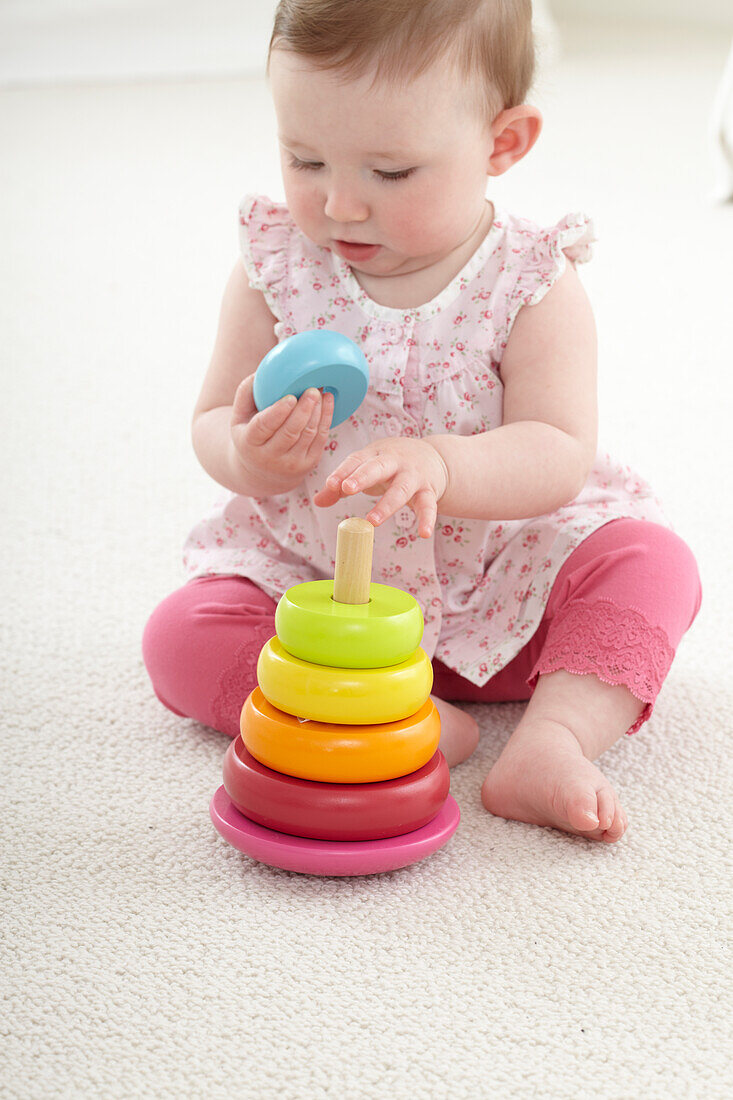 Baby girl sitting on floor playing with stacking rings