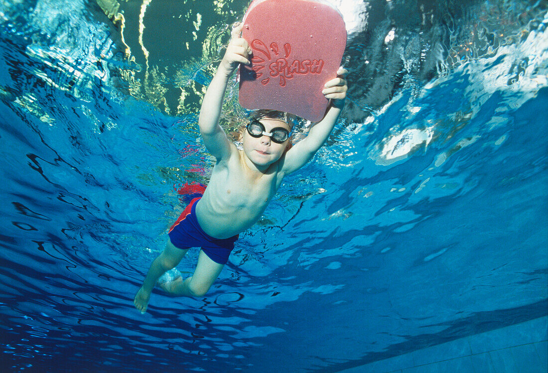 Boy holding onto a float board in a pool