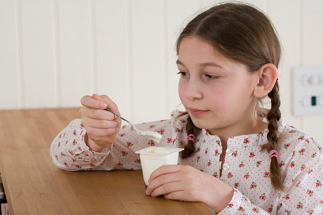 Girl sitting at table eating a yogurt