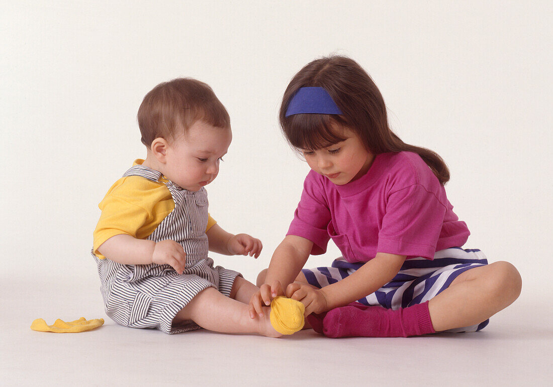 Girl putting on her baby brother's sock