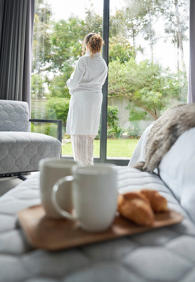 Woman in bathrobe standing at bedroom window
