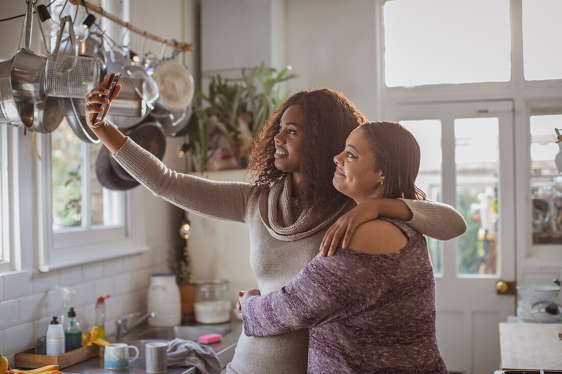 Mother and daughter taking selfie in kitchen