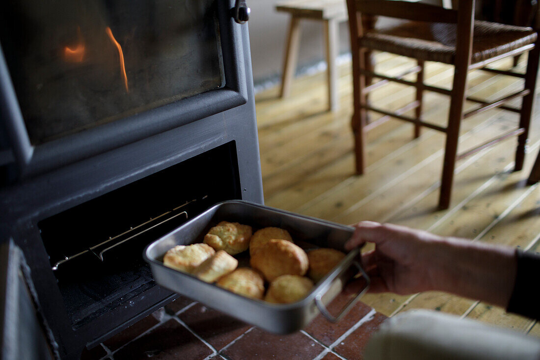 Man placing biscuits into stove oven in cabin