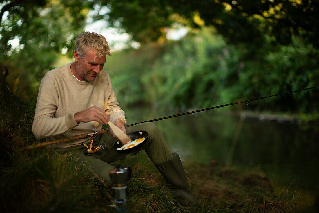 Man fly fishing and cooking eggs at riverbank