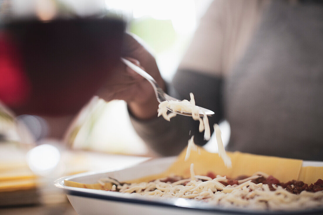 Woman sprinkling cheese over lasagne