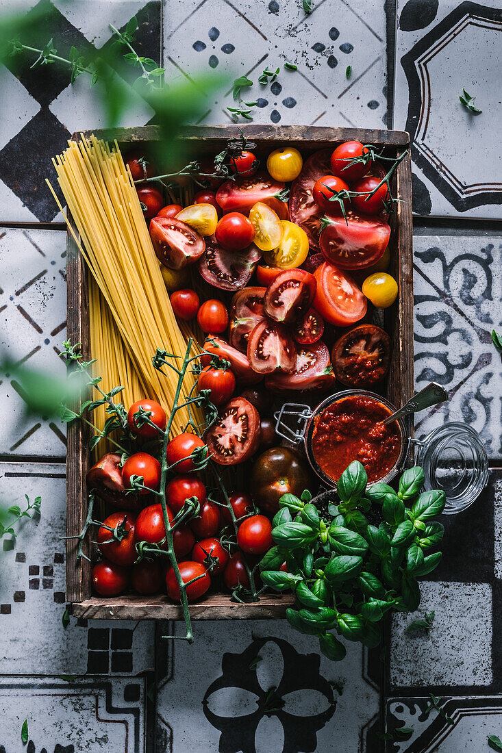 Colourful tomatoes, pesto rosso, spaghetti and basil in a rustic wooden box