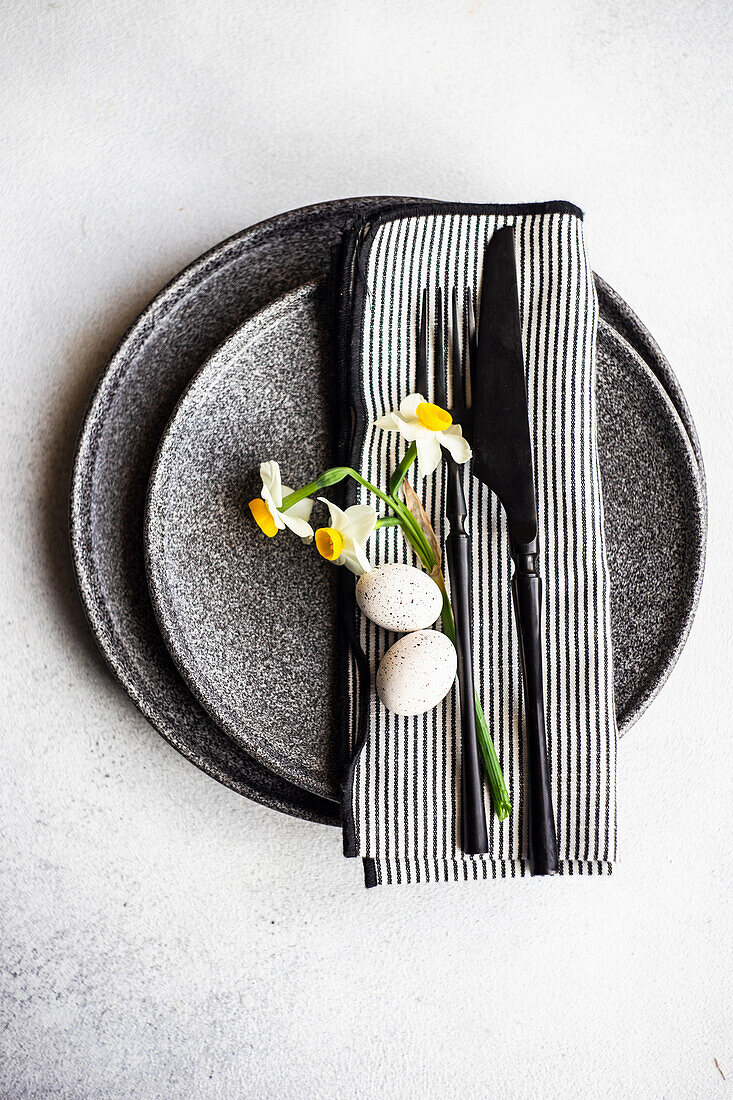 Place setting for Easter festive dinner with daffodil flowers and eggs on concrete background