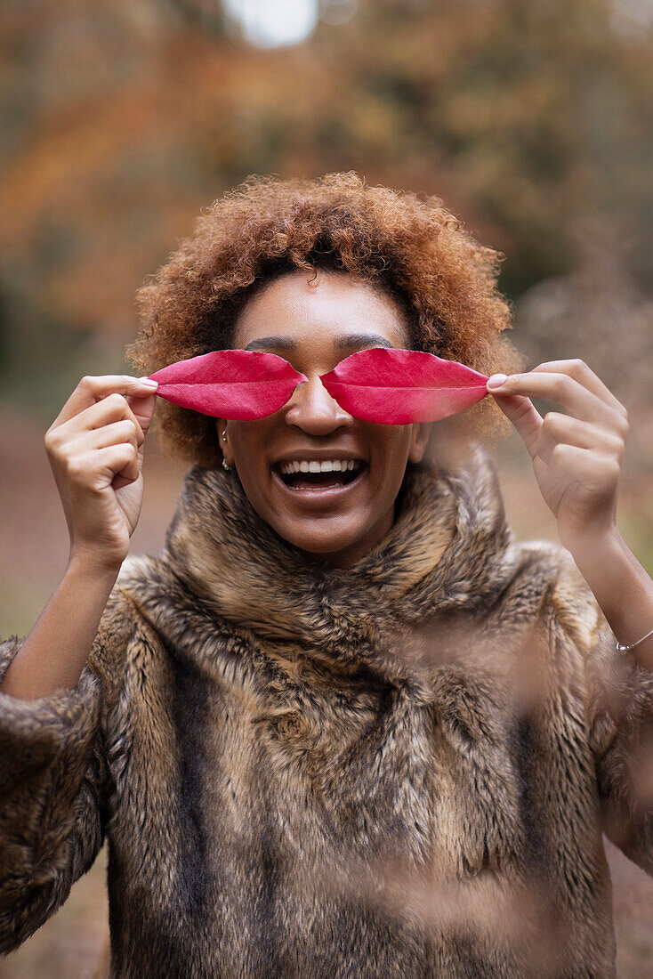 Playful young woman covering eyes with red autumn leaves