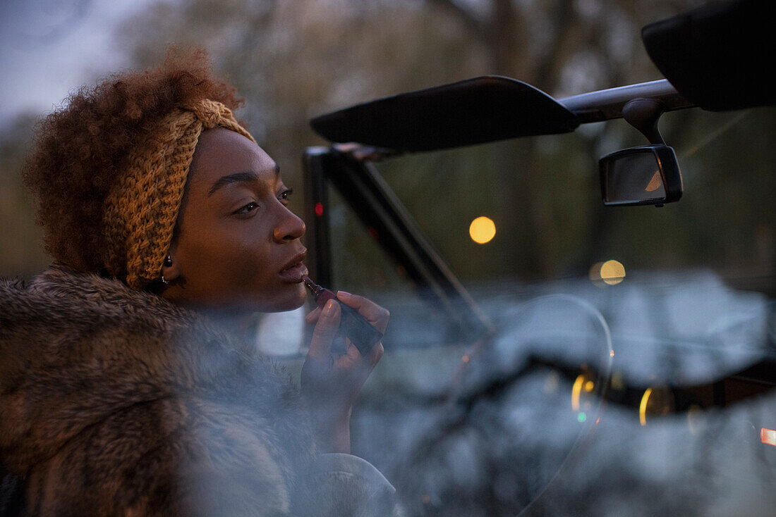 Young woman putting on lipstick in convertible at night