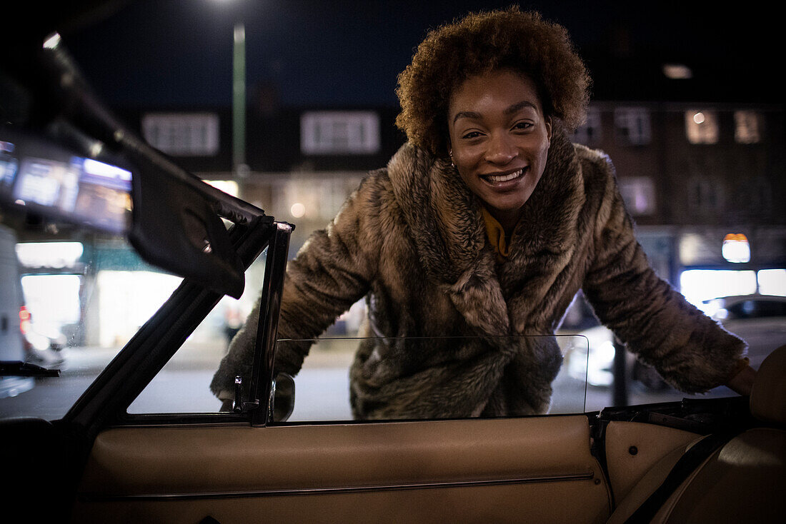 Happy young woman outside convertible at night