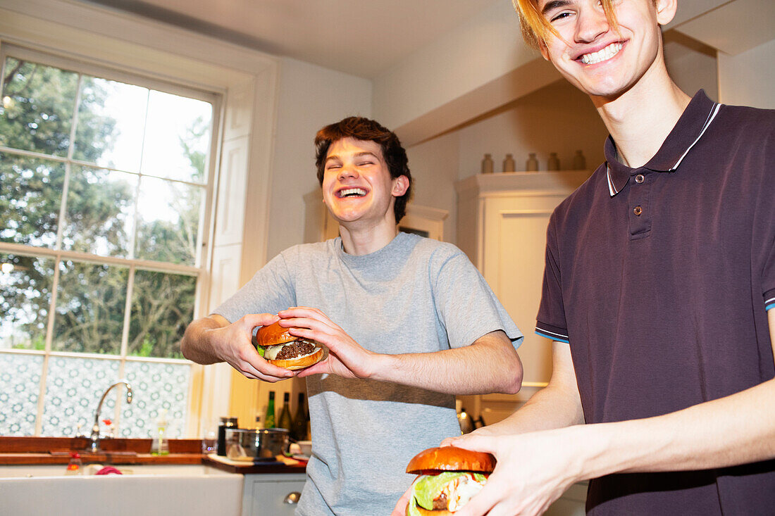 Happy teenage boys eating hamburgers in kitchen