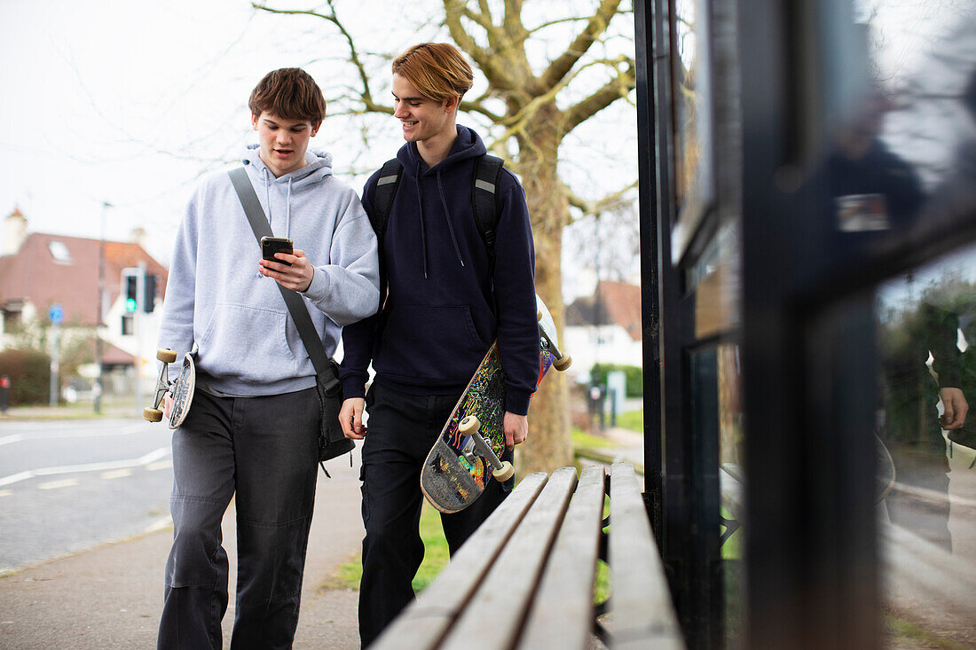 Teenage boys with skateboards and smartphone at bus stop