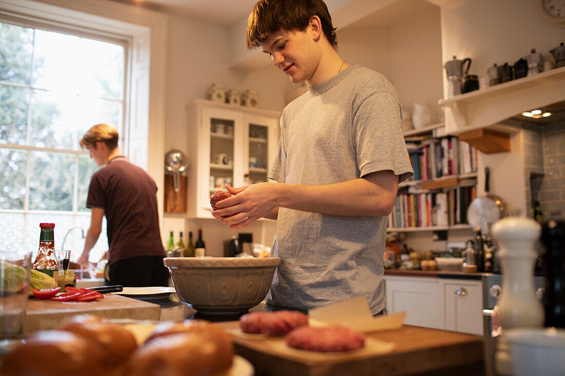 Teenage boy making hamburger patties in kitchen at home