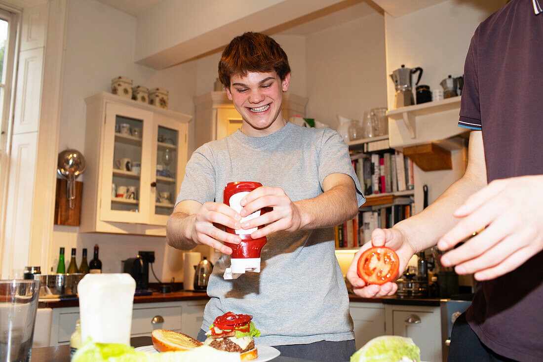 Happy teenage boy squeezing ketchup onto hamburger