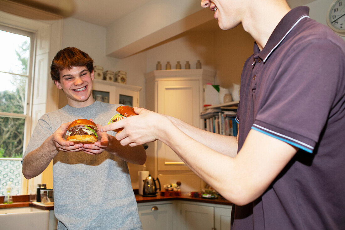 Happy teenage boys eating hamburgers at home