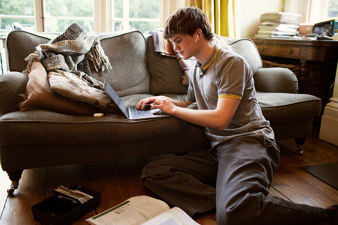 Focused teenage boy with laptop studying in living room
