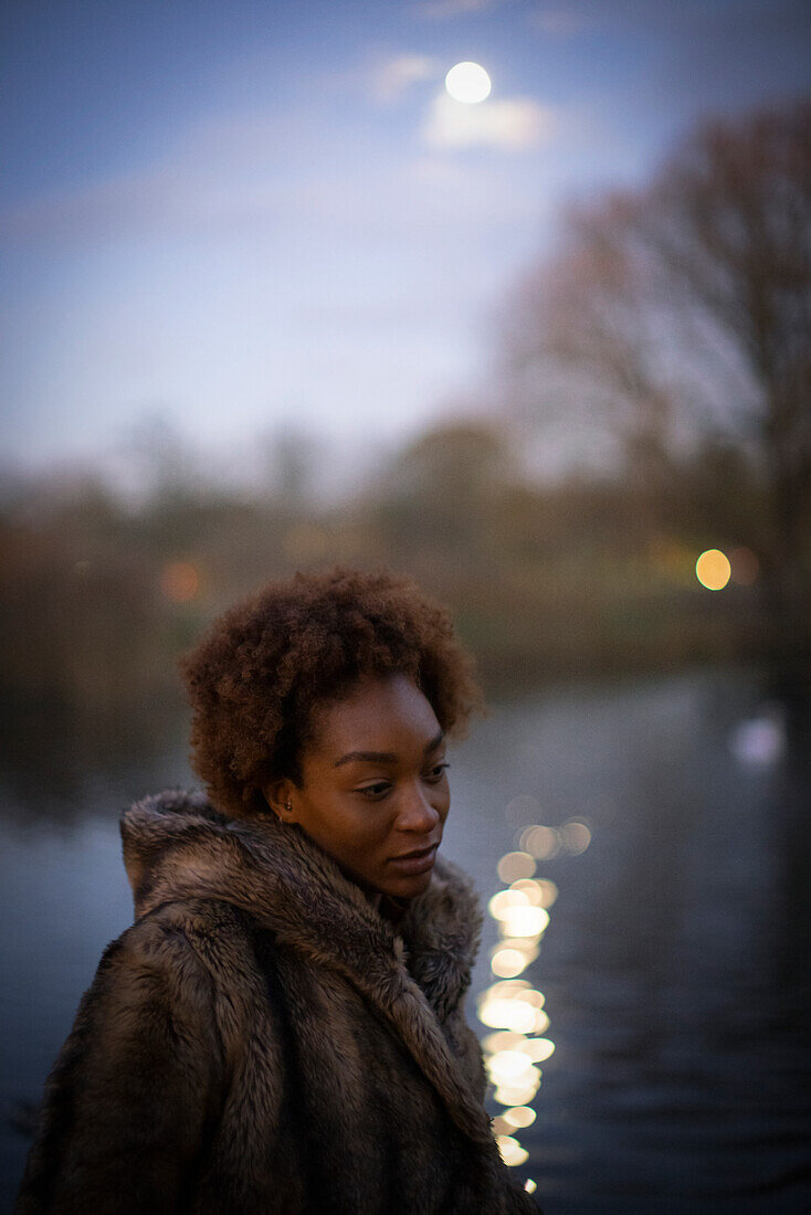 Woman walking along moonlit pond in park at night