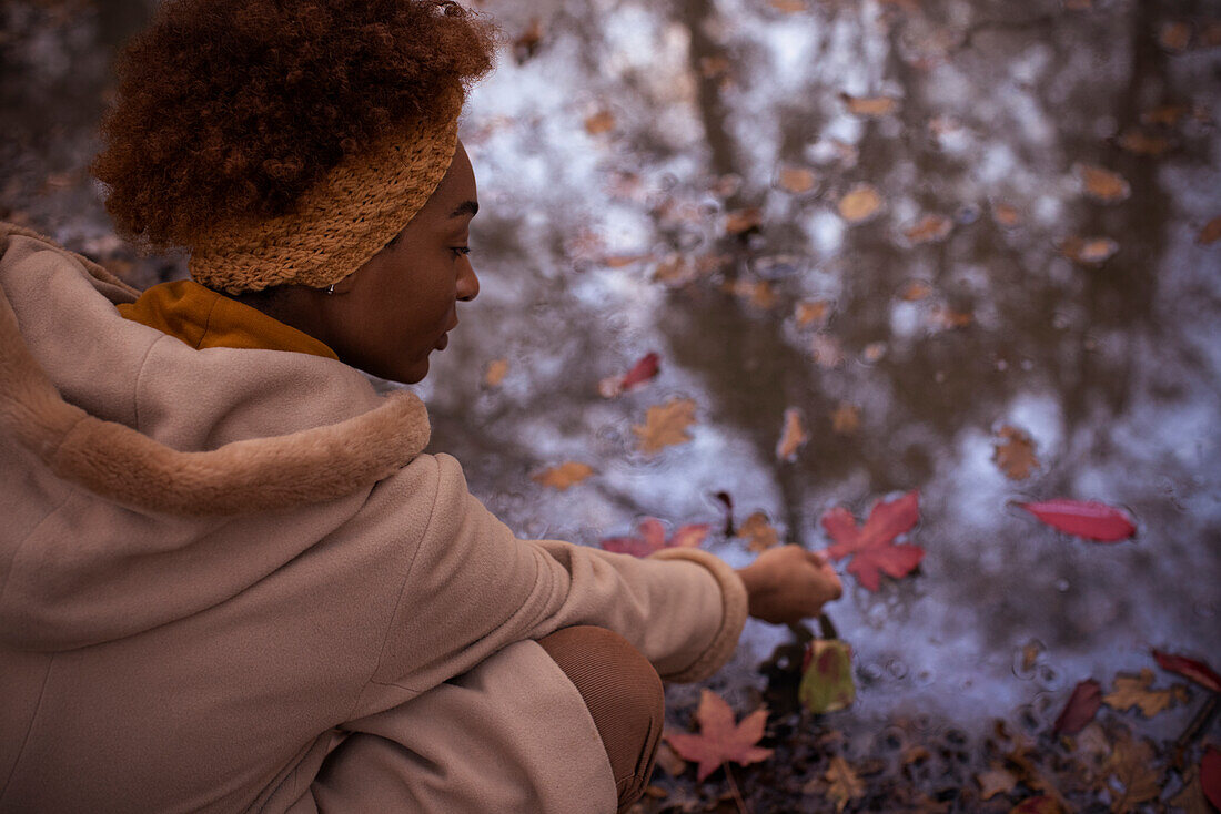 Young woman reaching for red autumn leaf in puddle