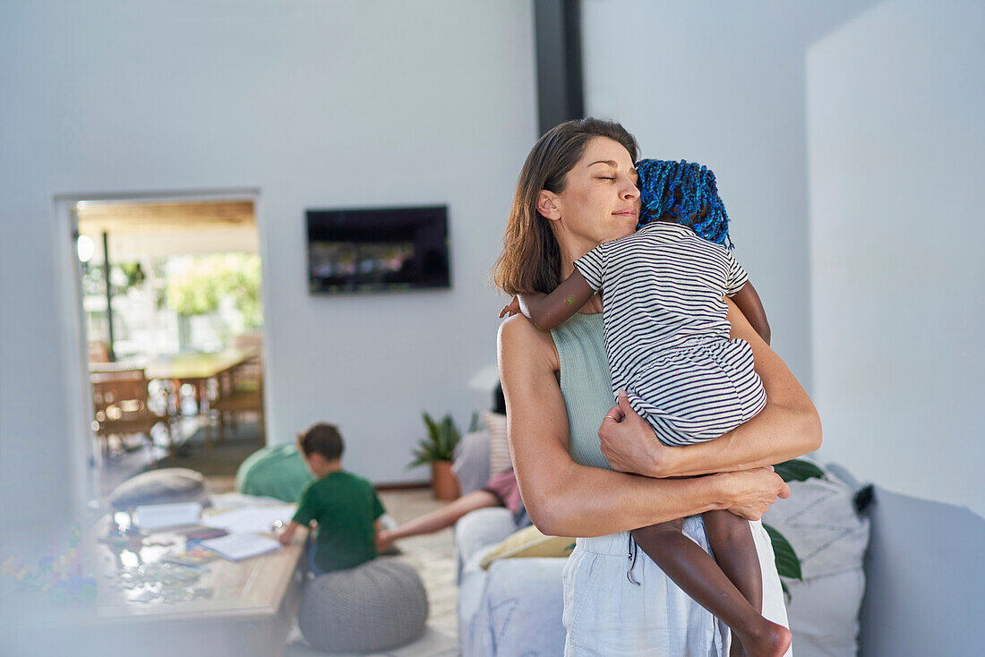 Serene mother holding toddler daughter at home