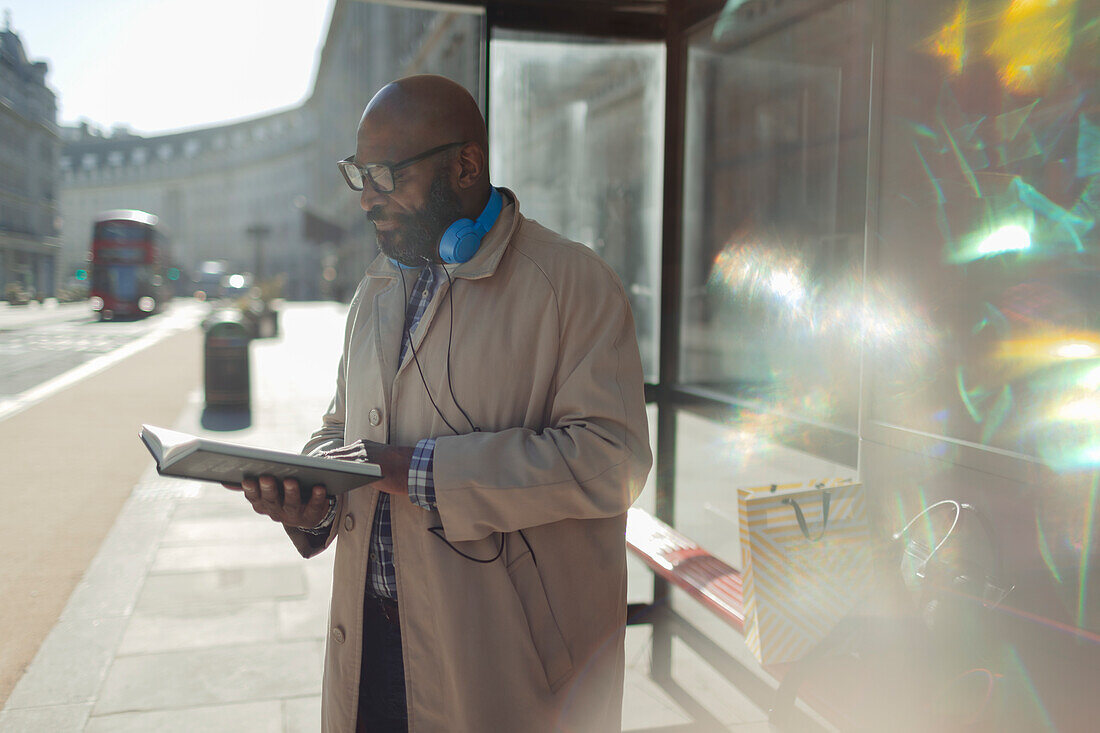 Businessman reading book at sunny city bus stop, London, UK