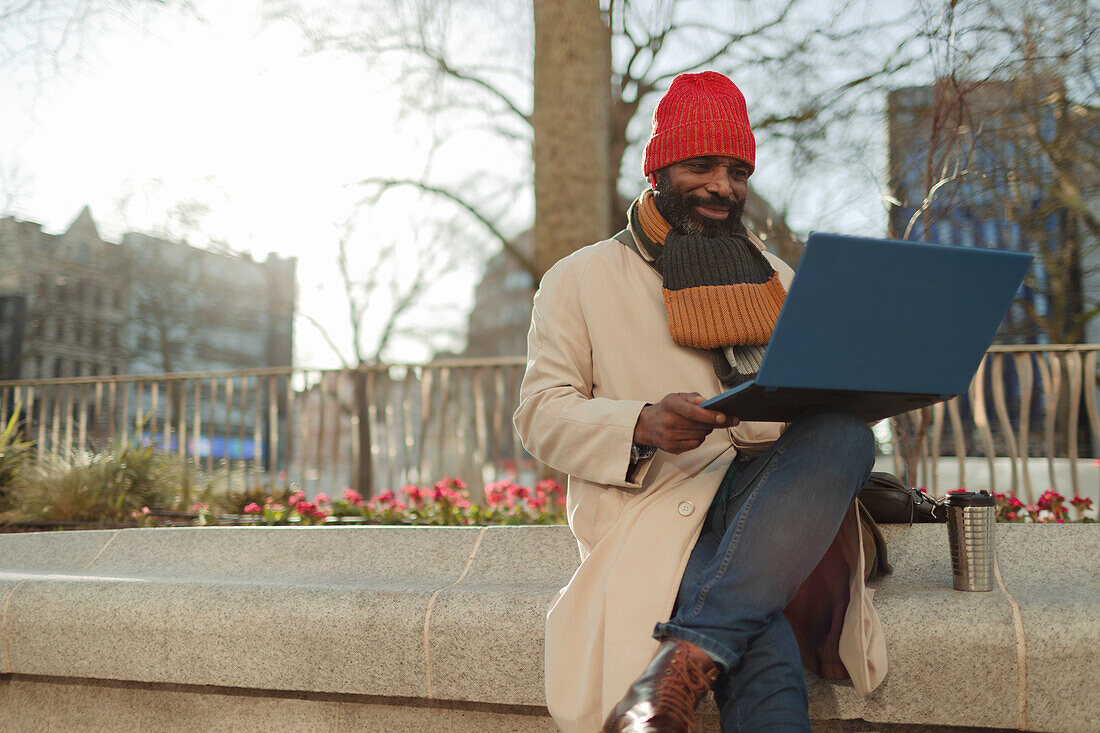 Businessman using laptop in sunny city park