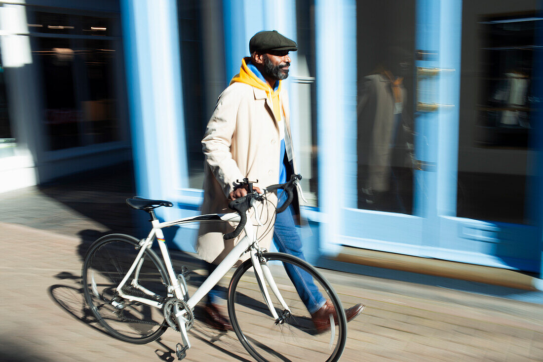 Man walking bicycle along sunny storefront