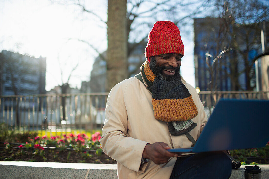 Man using laptop in sunny city park