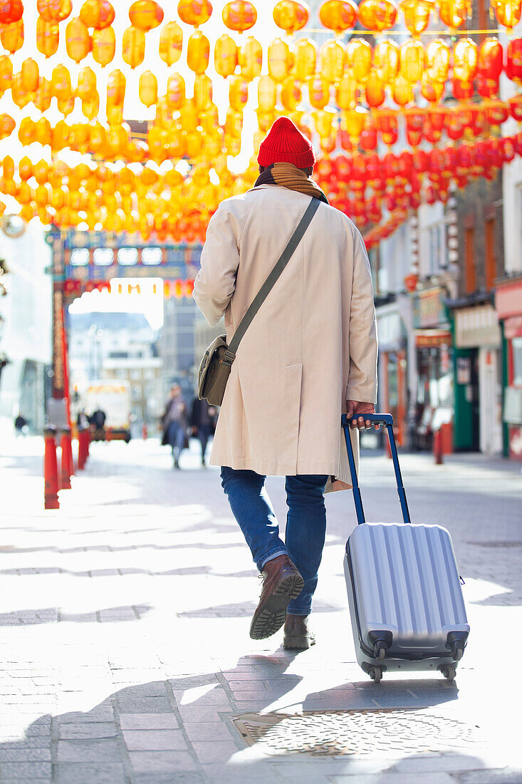 Male tourist pulling suitcase on sidewalk, London, UK