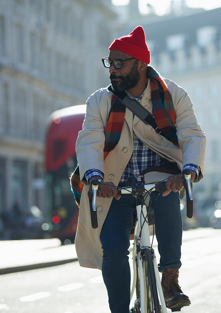 Businessman in stocking cap riding bike on sunny city street