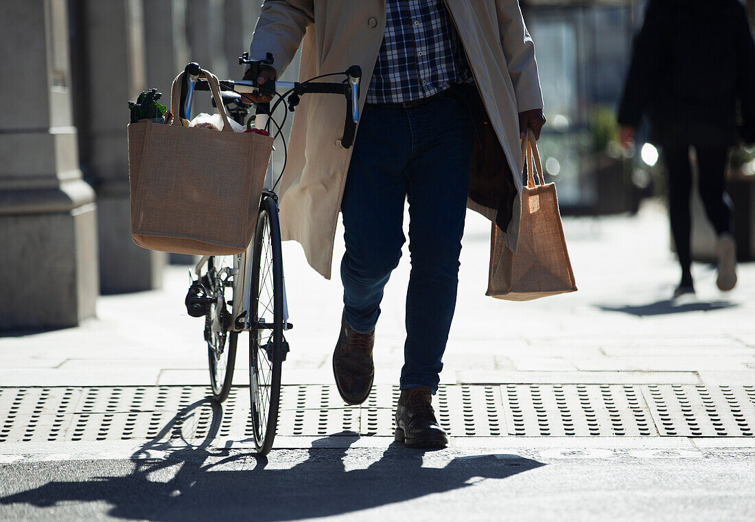 Man with bicycle and grocery bags walking on sidewalk