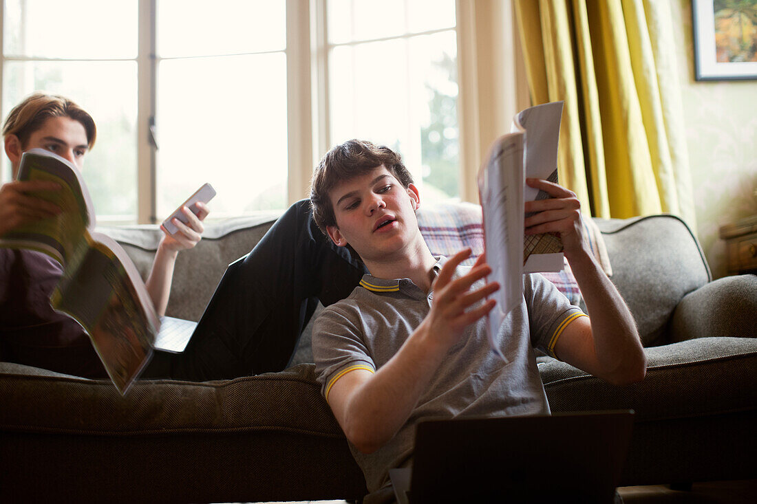 Teenage boys with textbooks studying on sofa at home