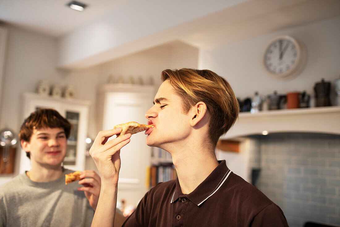 Hungry teenage boys eating pizza in kitchen