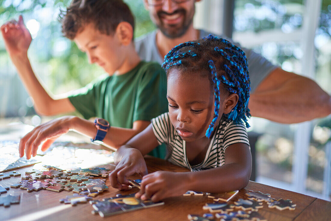 Toddler girl assembling jigsaw puzzle with family at table