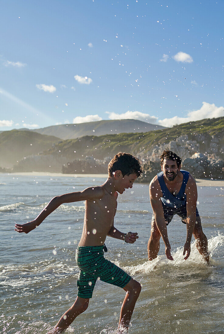 Happy playful father splashing son in sunny summer ocean