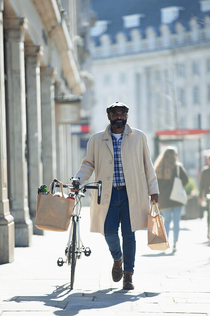 Man with bicycle and grocery bags walking on sunny sidewalk