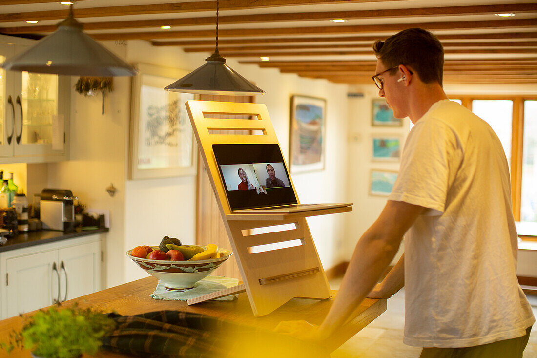 Man video conferencing on laptop stand desk in kitchen