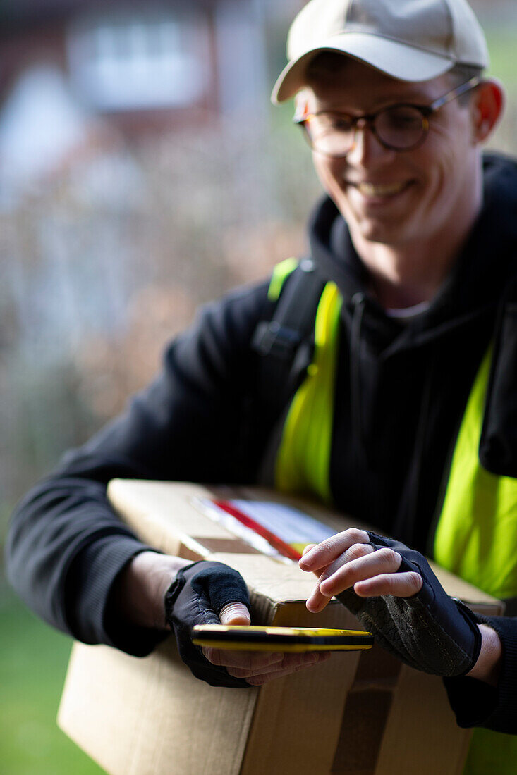 Smiling male courier with smartphone delivering package