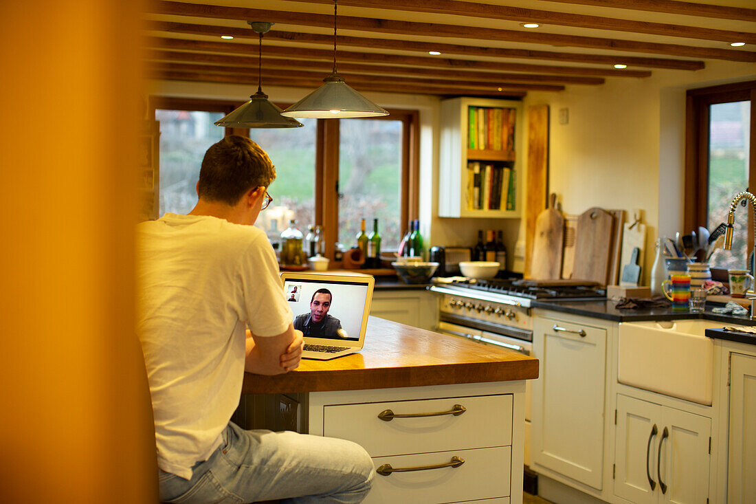 Man video conferencing with colleagues at laptop in kitchen