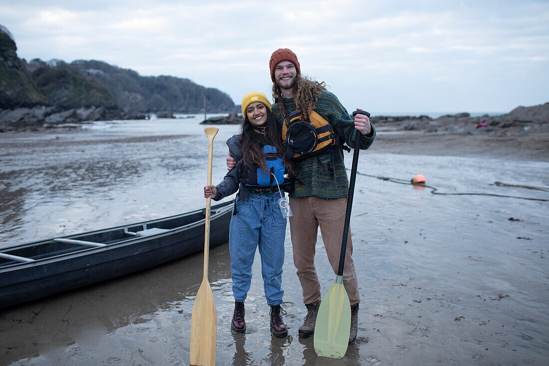 Happy couple with canoe and oars on beach