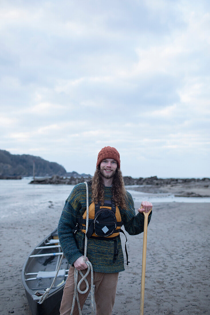 Smiling young man with canoe on beach