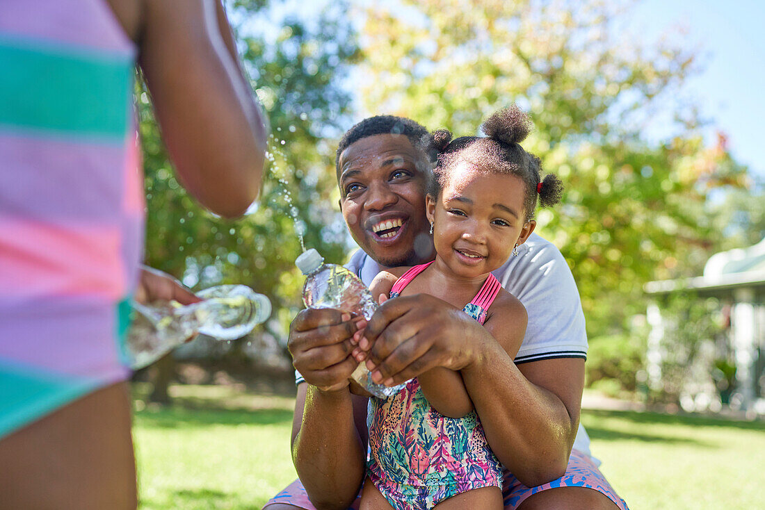 Happy father and daughters playing with squirt water bottles