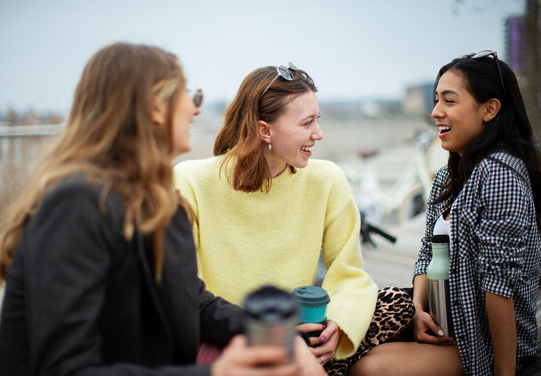 Happy young female friends talking and drinking coffee