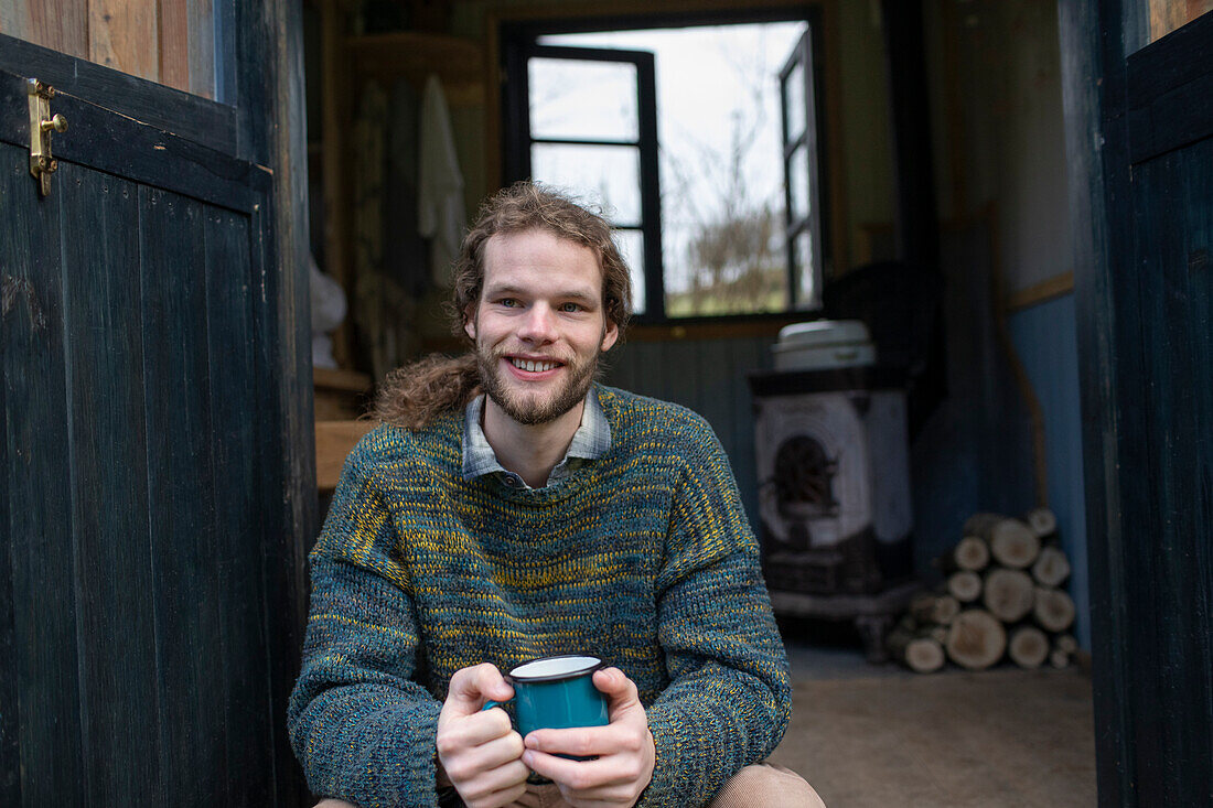 Happy young man drinking coffee in tiny cabin doorway